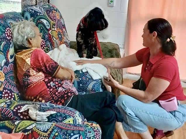 Woman and elderly lady with therapy dog indoors