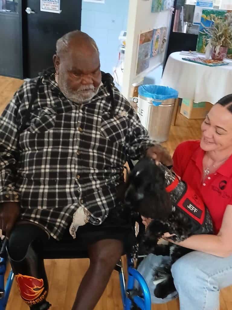 Man in wheelchair patting therapy dog with carer