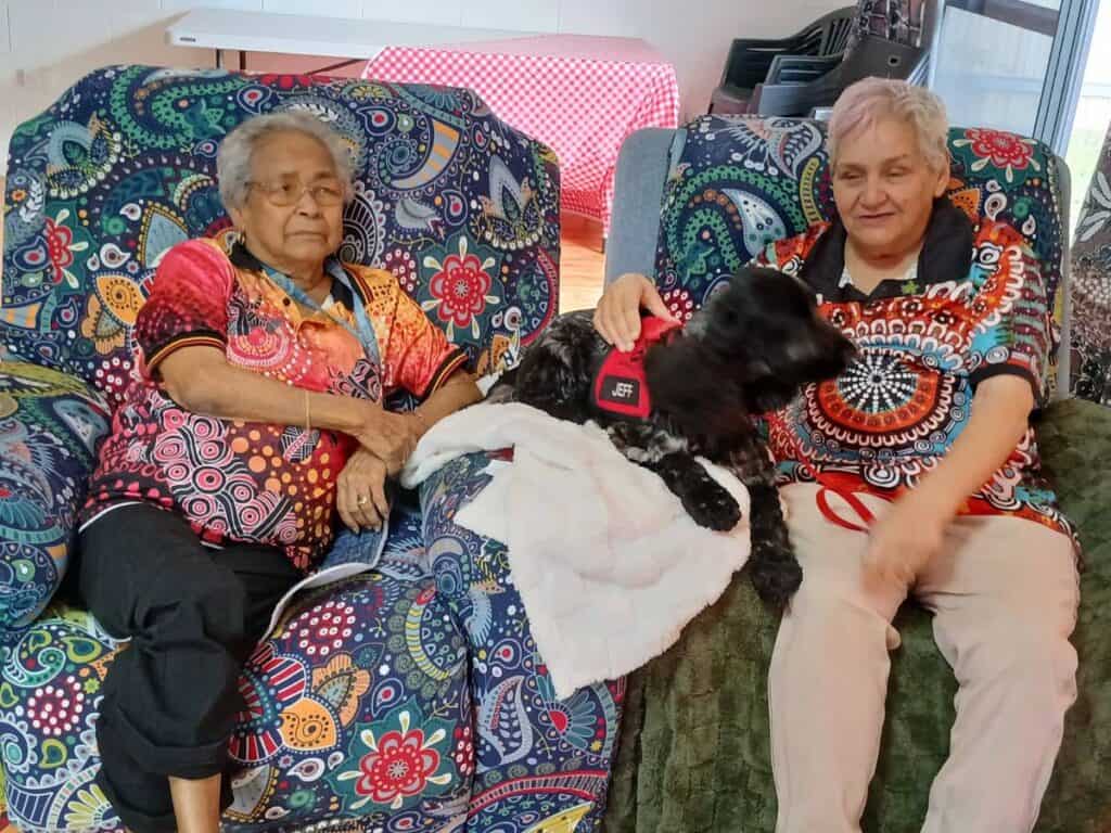 Two women sitting with a therapy dog indoors